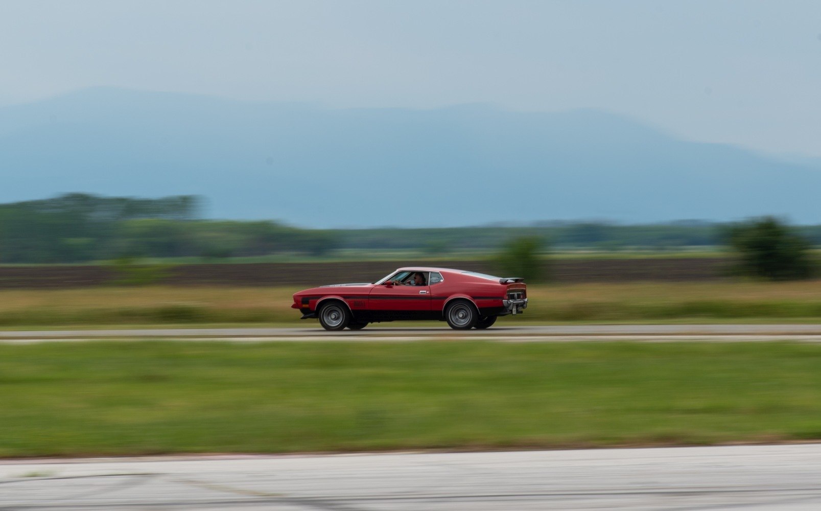 Side view of red muscle car speeding on rural road