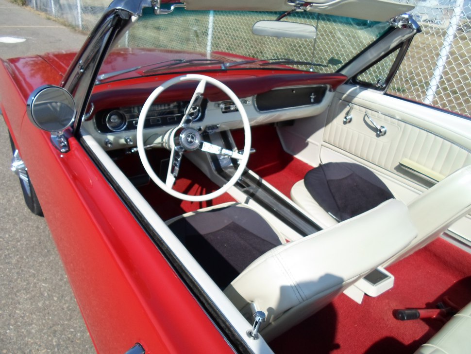 Classic white steering wheel and red carpet interior of a vintage convertible car