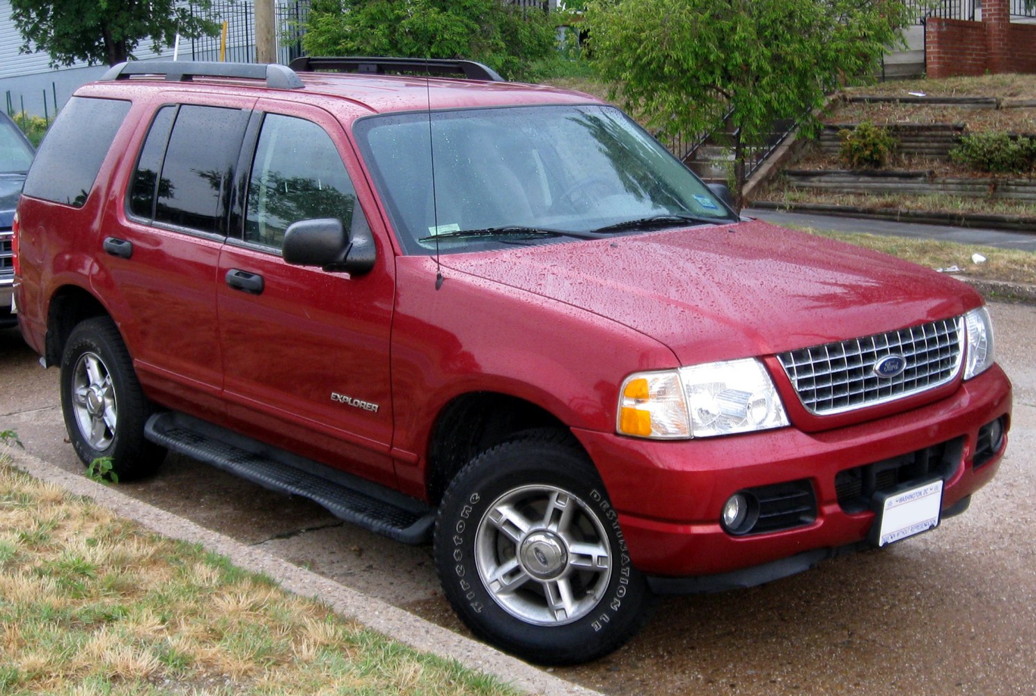 Red SUV with chrome grille, side steps, alloy wheels, and roof rails