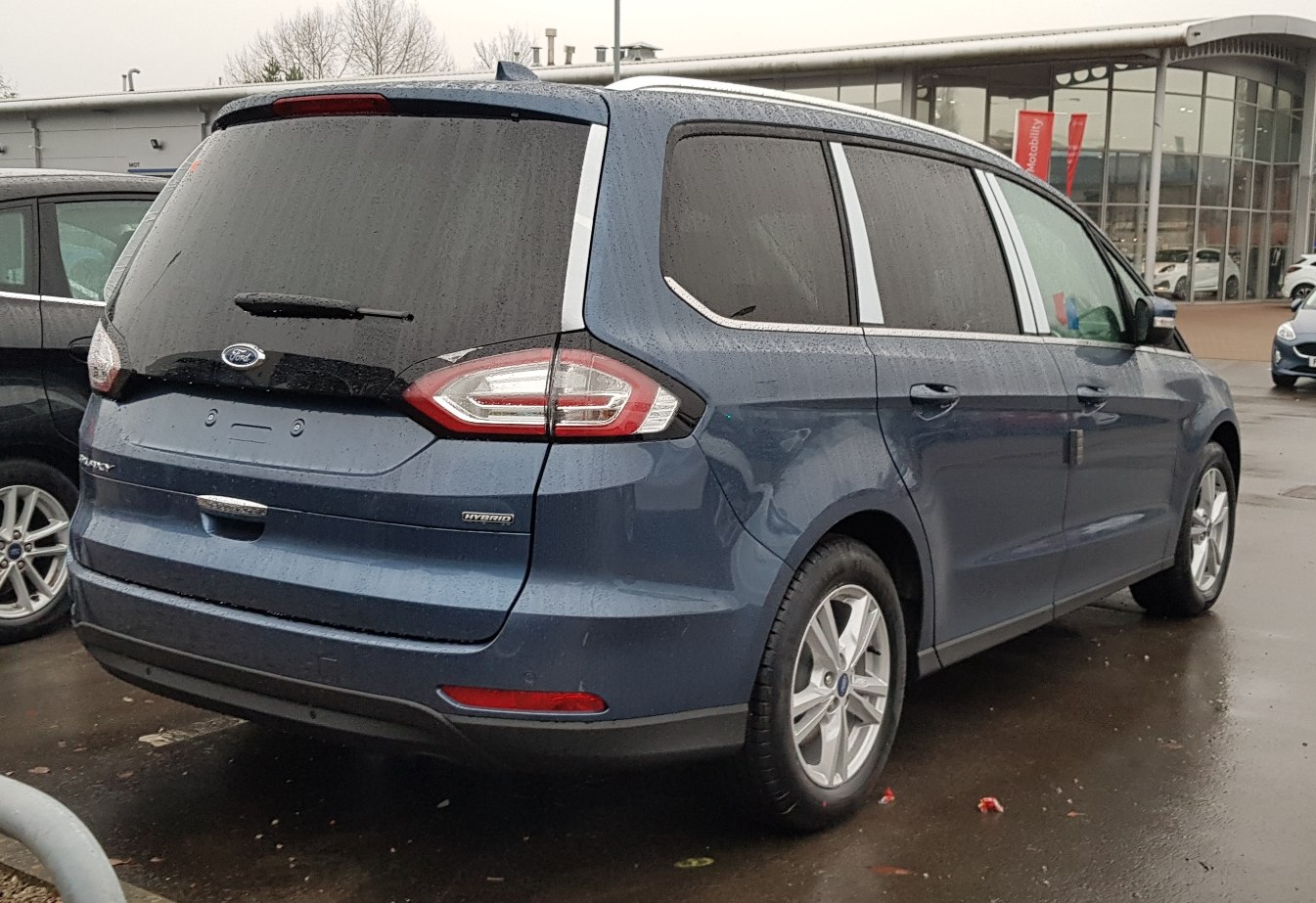 Rear view of blue modern minivan with hybrid badge and distinctive taillights