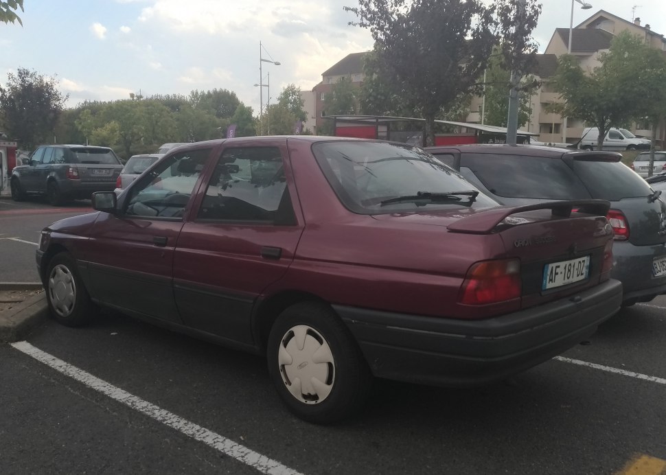 Rear and side view of a maroon sedan with rear spoiler and hubcaps