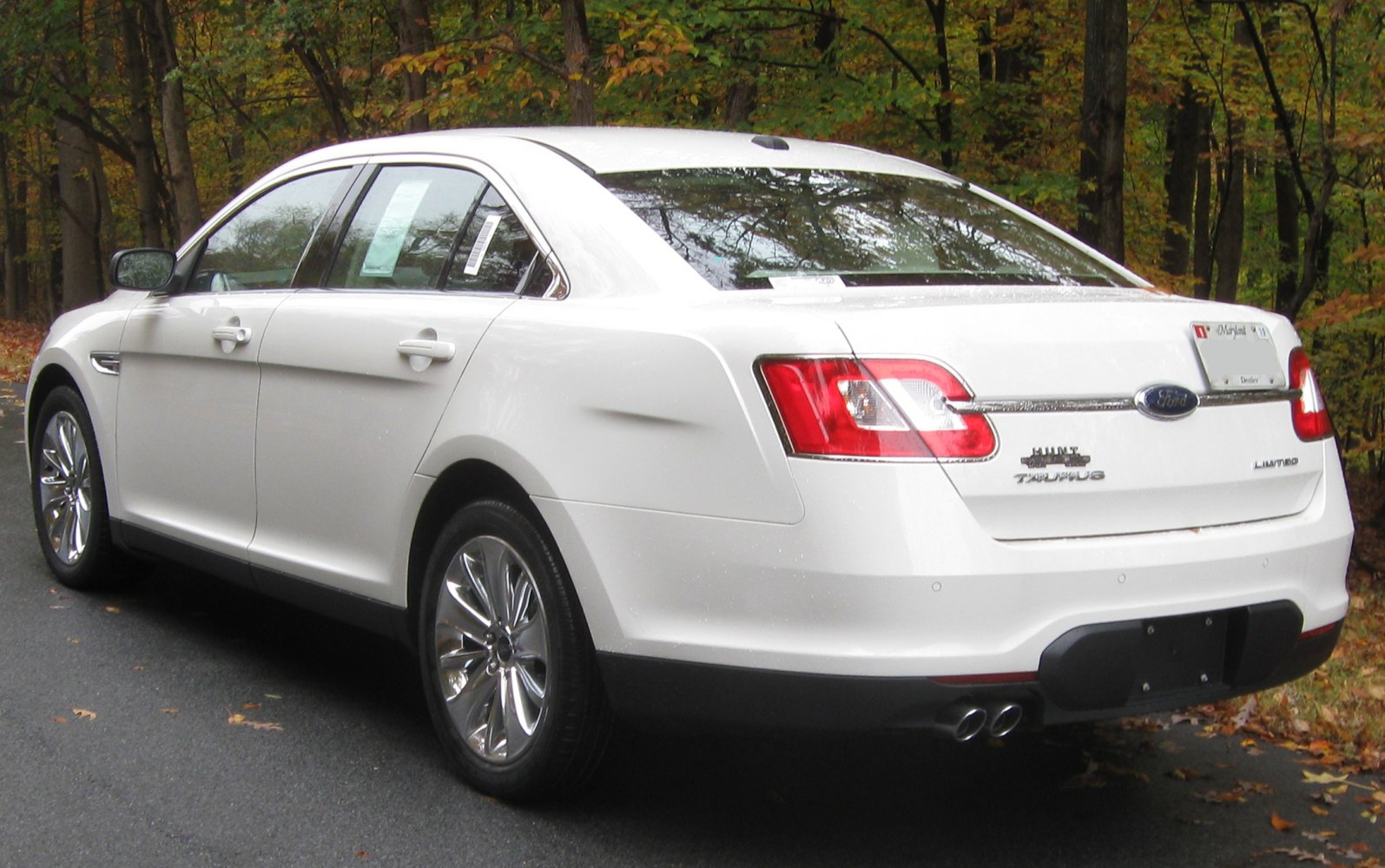Rear side profile of a white sedan with chrome wheels and dual exhaust