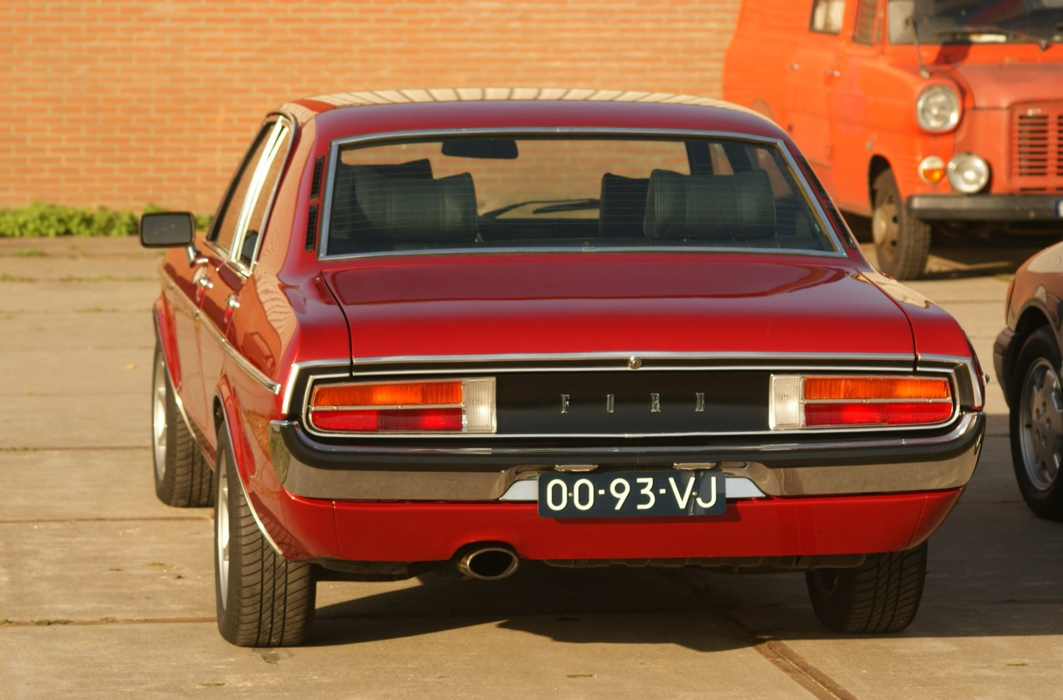 Rear view of vintage red sedan with distinct tail lights and rear window.
