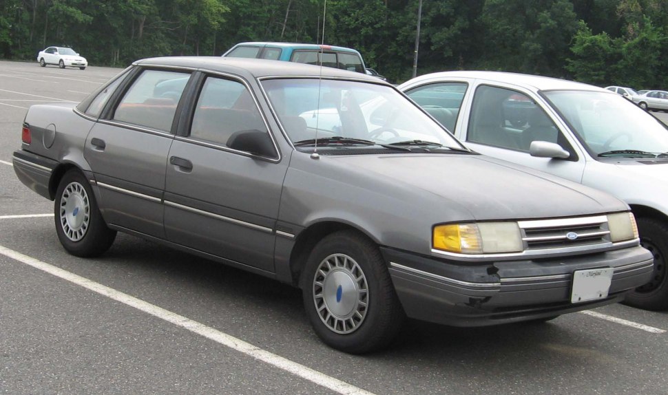 Front-side view of a gray compact four-door sedan with 1980s styling and hubcaps.