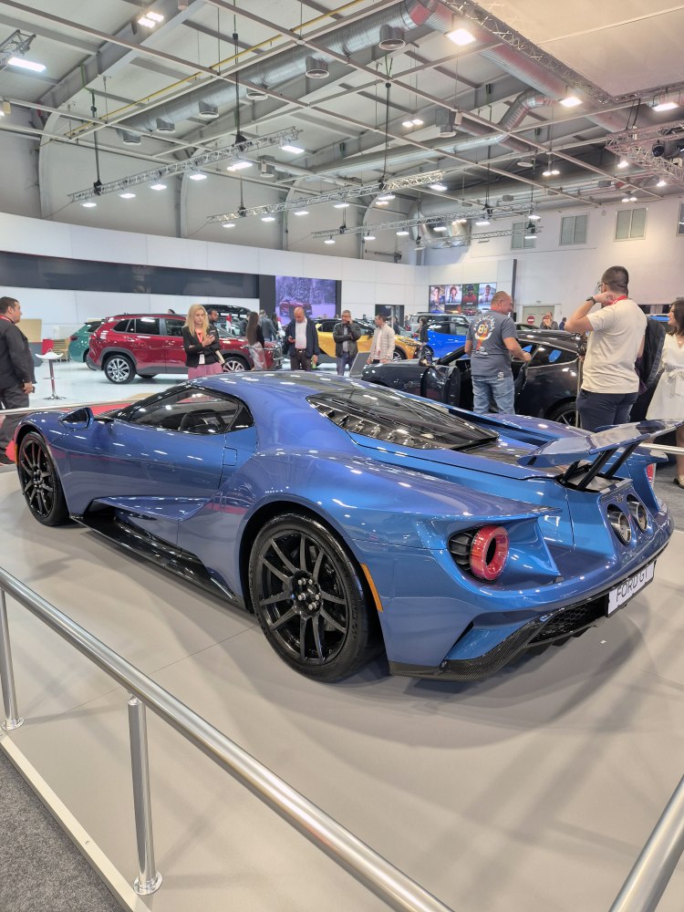 Blue sports car rear-side view with large rear wing and black wheels