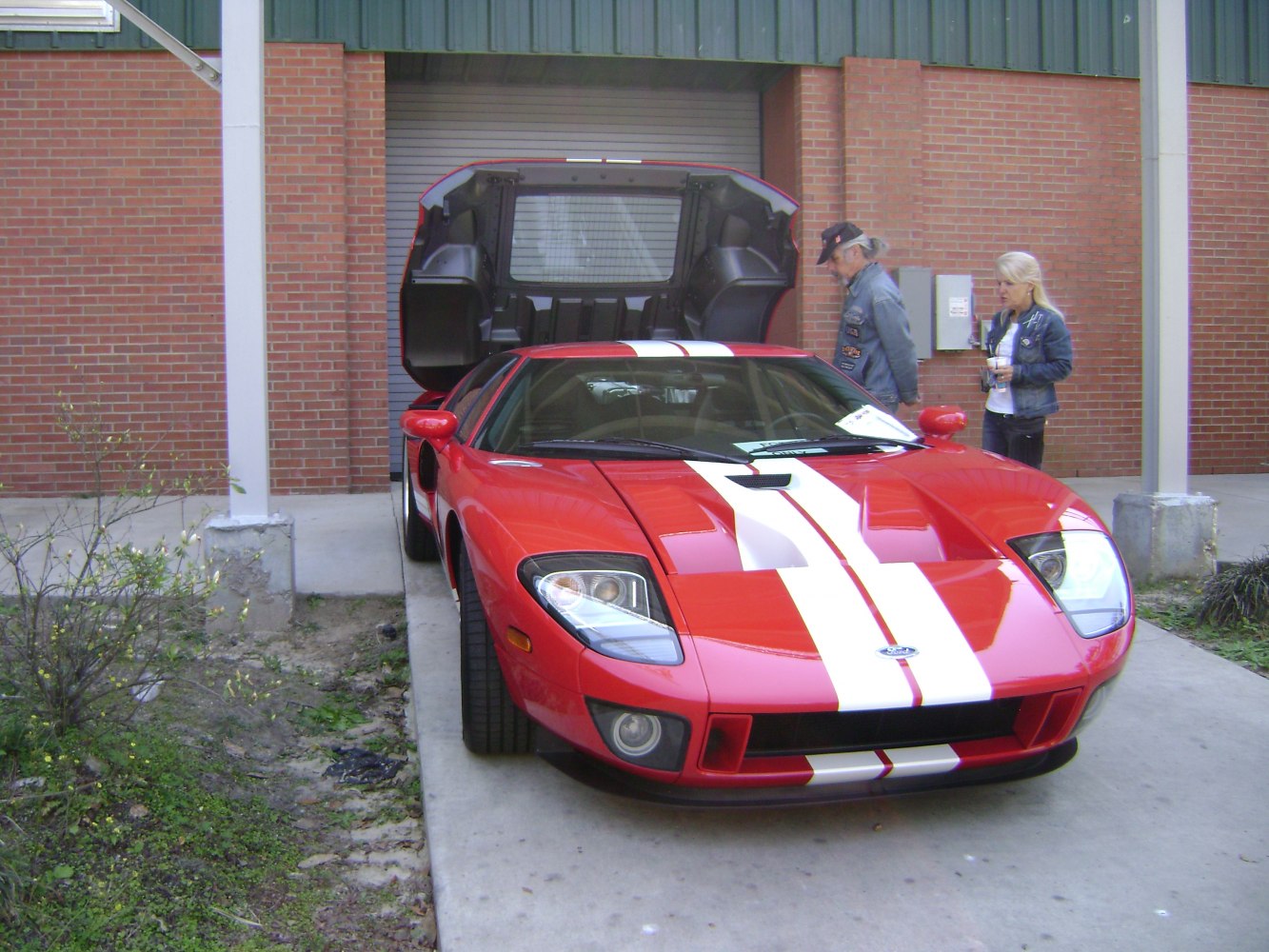 Red sports car with white racing stripes and rear hatch open.