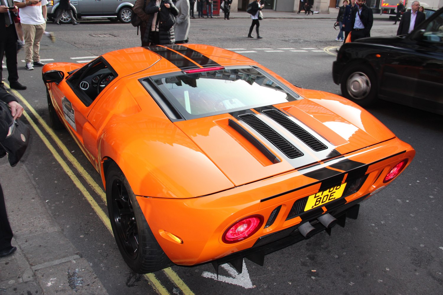 Orange sports car rear with black racing stripes and engine bay vents