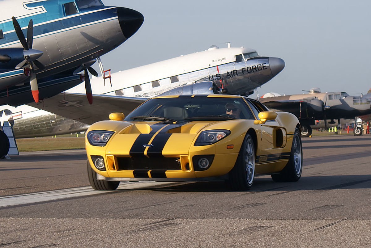 Yellow sports car with black stripes, front view, at an airfield
