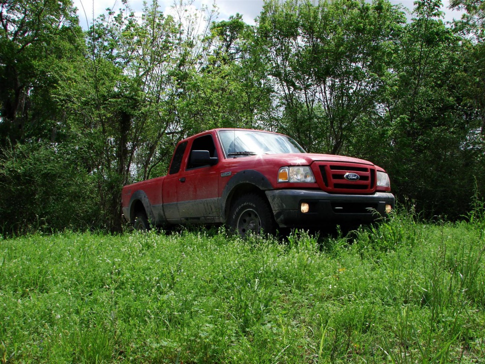 Red pickup truck with extended cab parked on grassy terrain.