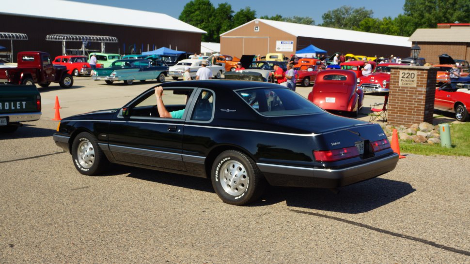 Rear three-quarter view of a black 1980s sedan with distinct tail lights and alloy wheels.
