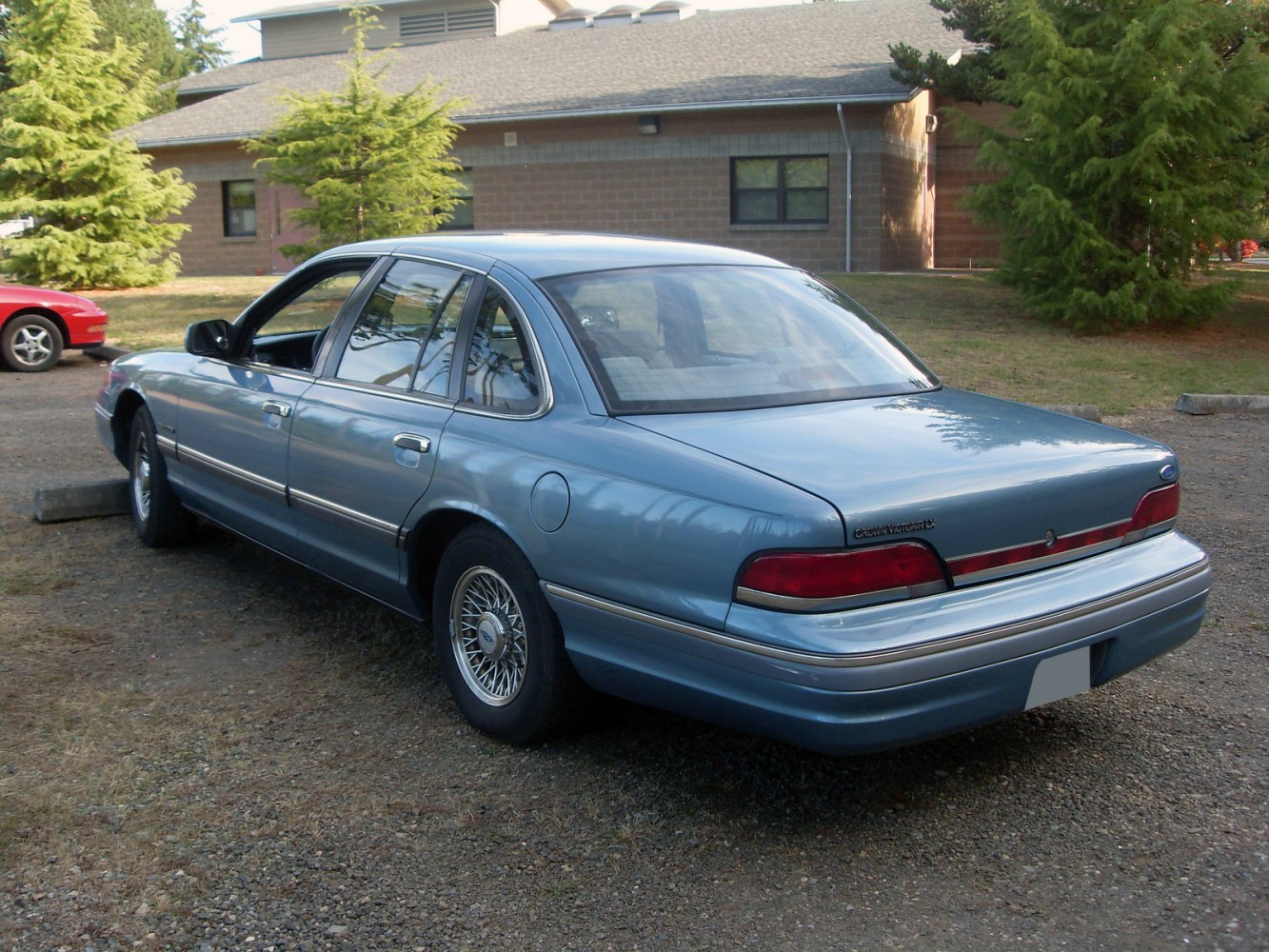 Rear and side profile of a light blue sedan with wire-spoke wheels.