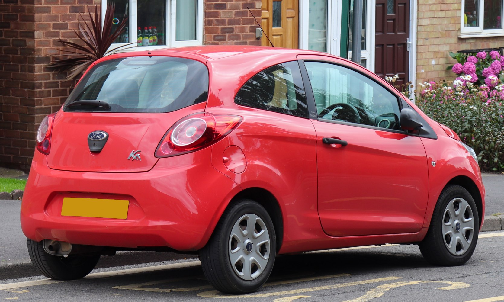 Rear side view of a red compact 3-door hatchback car with distinctive circular taillights.