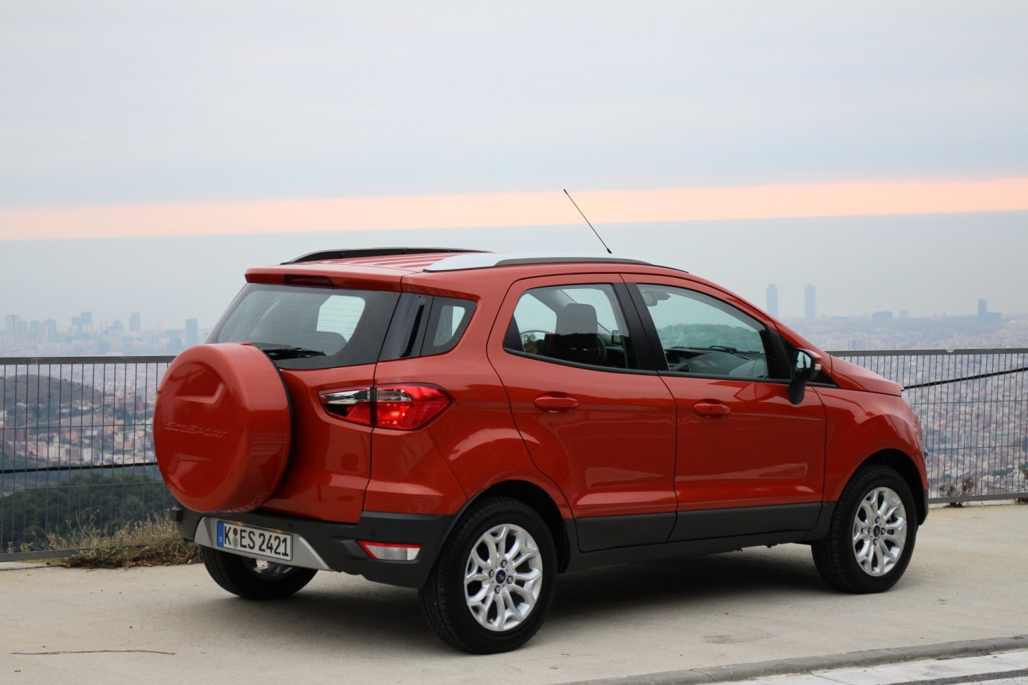 Rear and side view of orange compact SUV with spare tire cover and roof rails