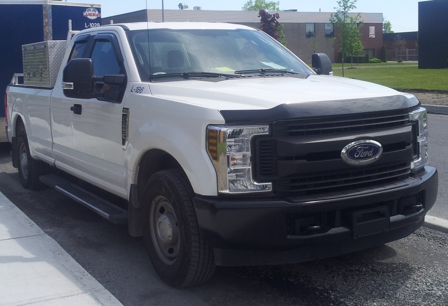 White pickup with super cab, long bed, black grille, and front headlights.