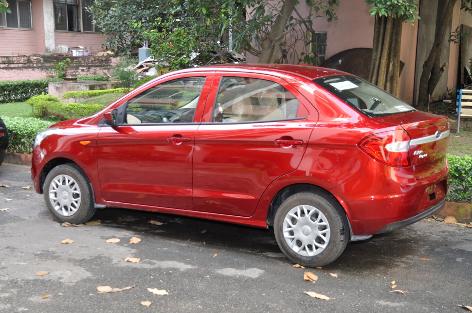 Side profile of a red compact sedan with rear design and wheel covers.