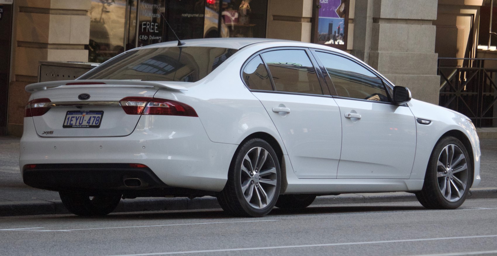 Rear side view of white sedan with spoiler and alloy wheels