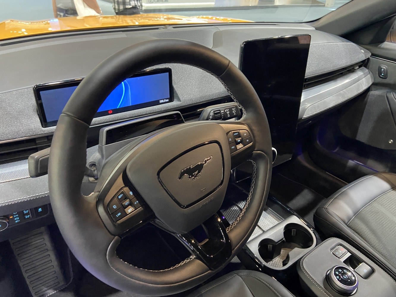 Steering wheel with control buttons and two digital screens on dashboard.