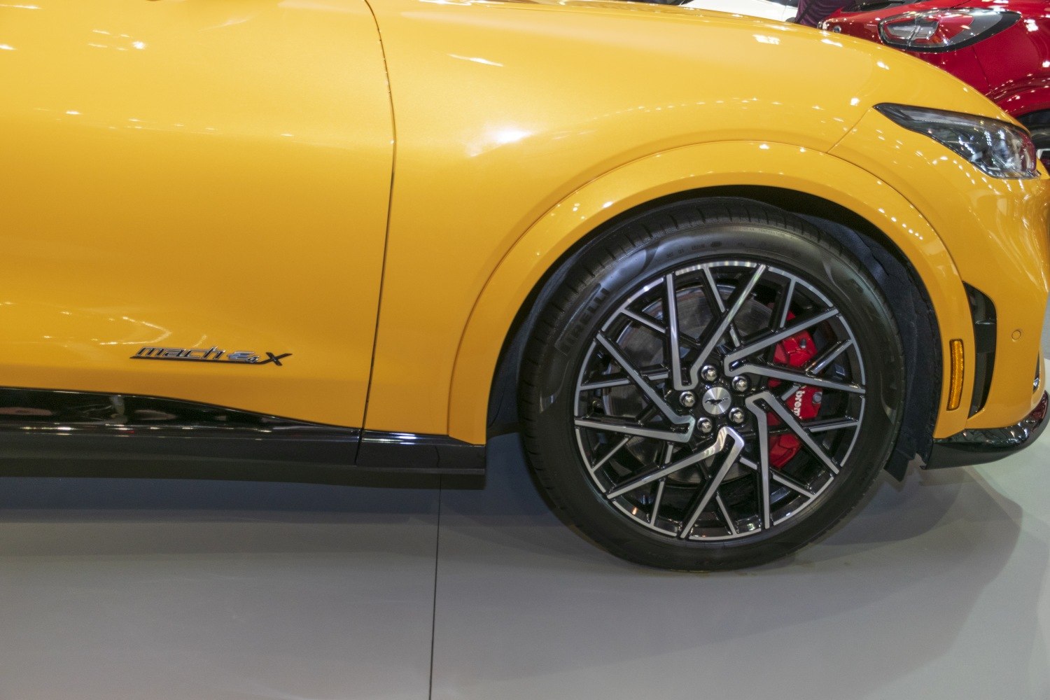 Yellow vehicle side panel with Mach-E X badge and black multi-spoke alloy wheel with red brake caliper