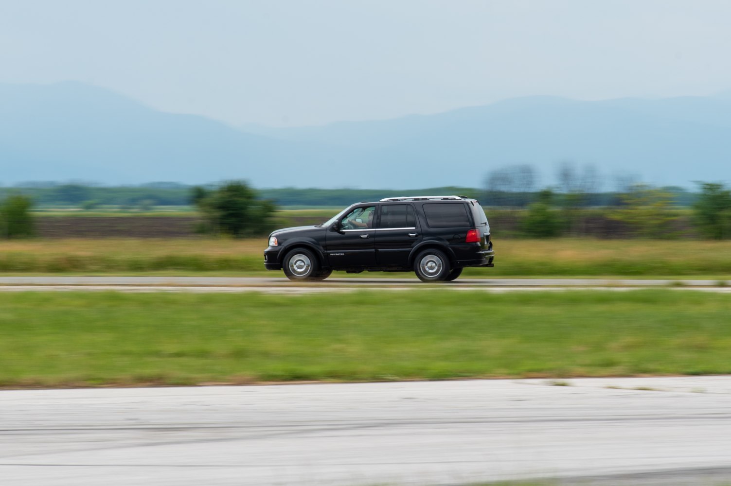 Black large SUV driving fast on rural road side view