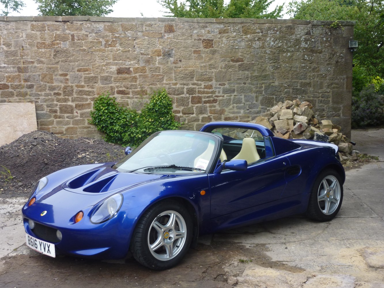 Blue lightweight roadster with targa roof and sporty side air intakes.