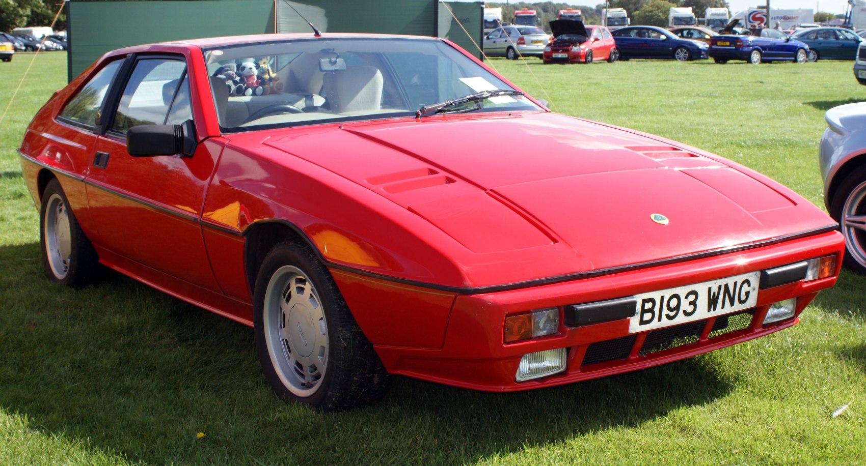 Angular front side profile of a red vintage sports coupe with side mirrors and pop-up headlights.