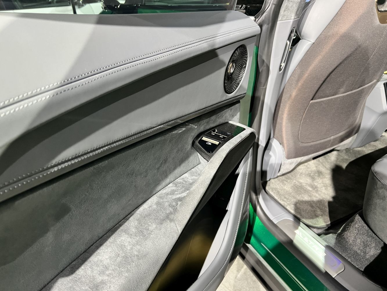 Car door interior panel with speaker, window controls, and stitching