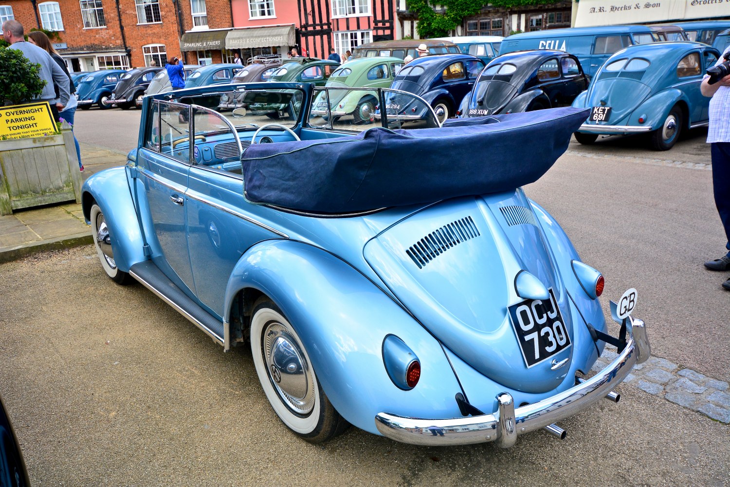 Light blue vintage convertible with folded soft top and whitewall tires