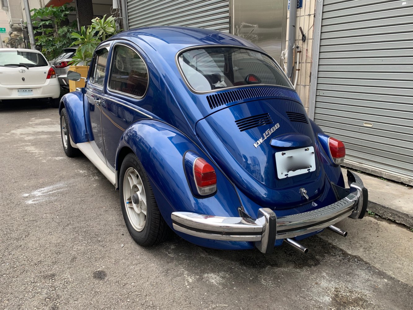 Rear view of a vintage rounded car with dual exhaust pipes and chrome bumper