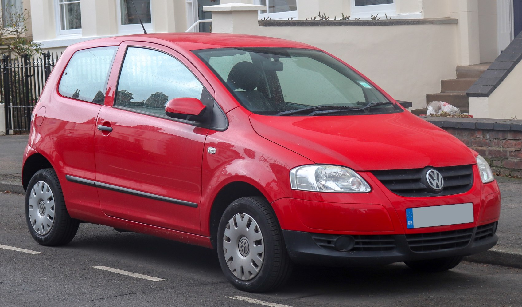 Red compact hatchback with 3-door layout and hubcap wheels