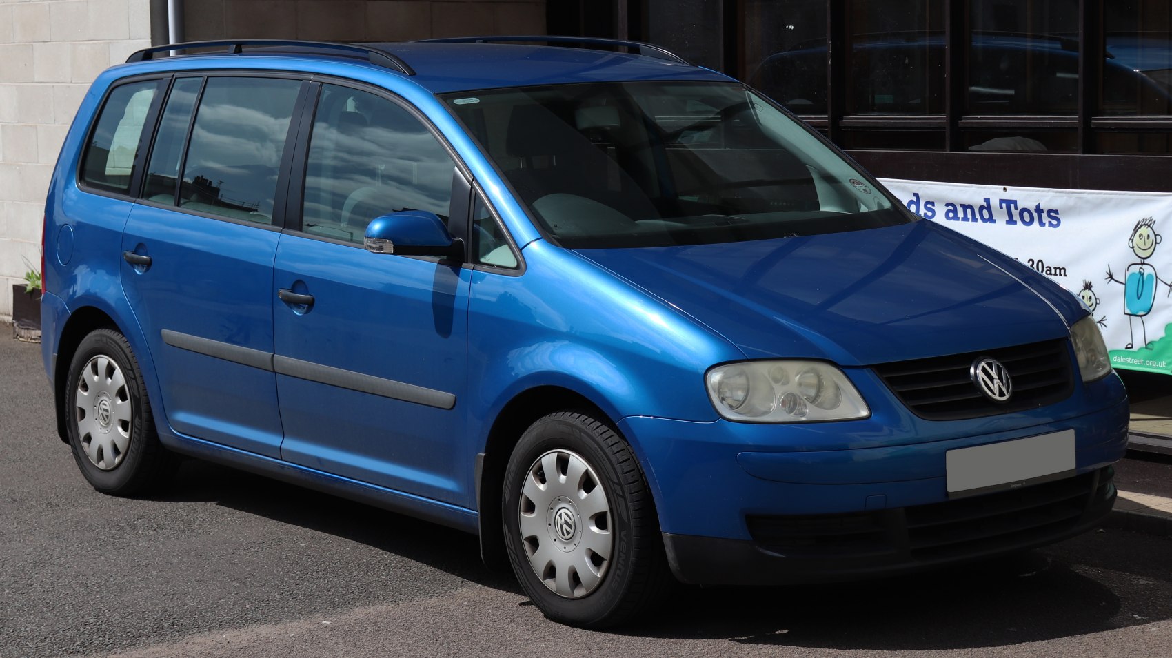 Blue five-door MPV with roof rails and classic halogen headlights front side view