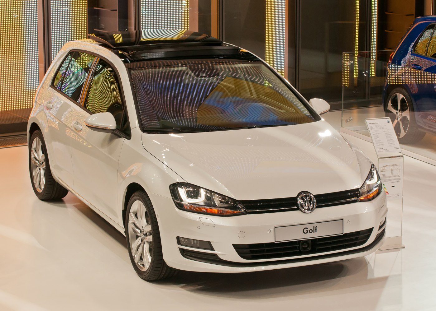 White hatchback with panoramic sunroof and LED headlights under showroom lighting