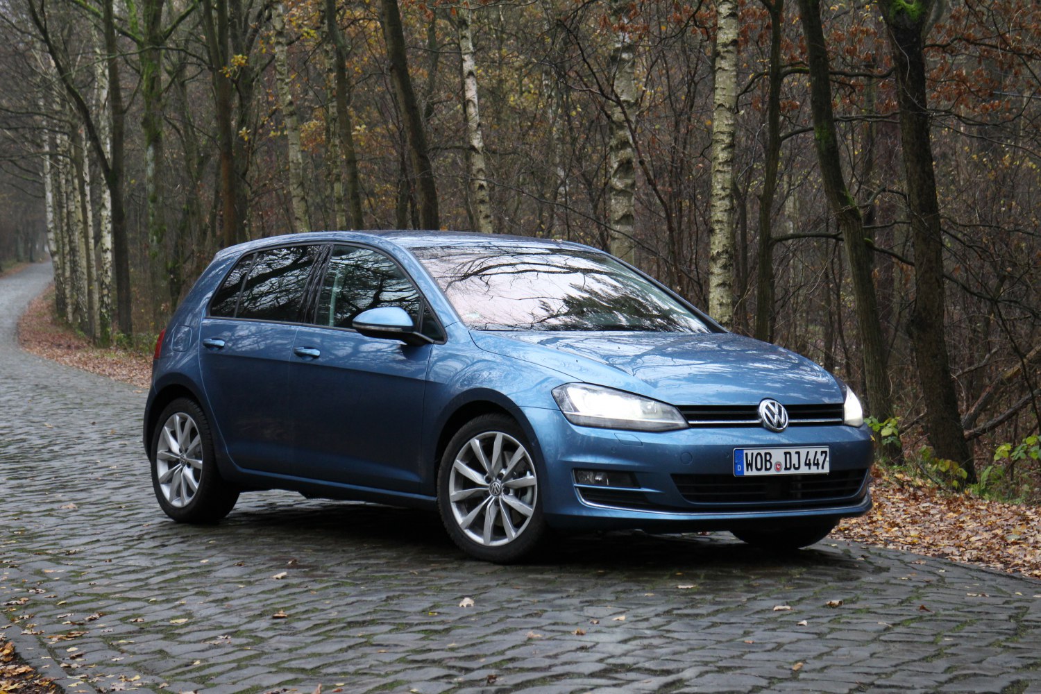 Front side view of a blue 5-door hatchback on cobblestone road