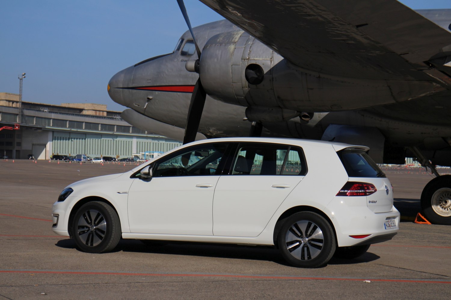 White 5-door compact hatchback with black alloy wheels parked near vintage plane