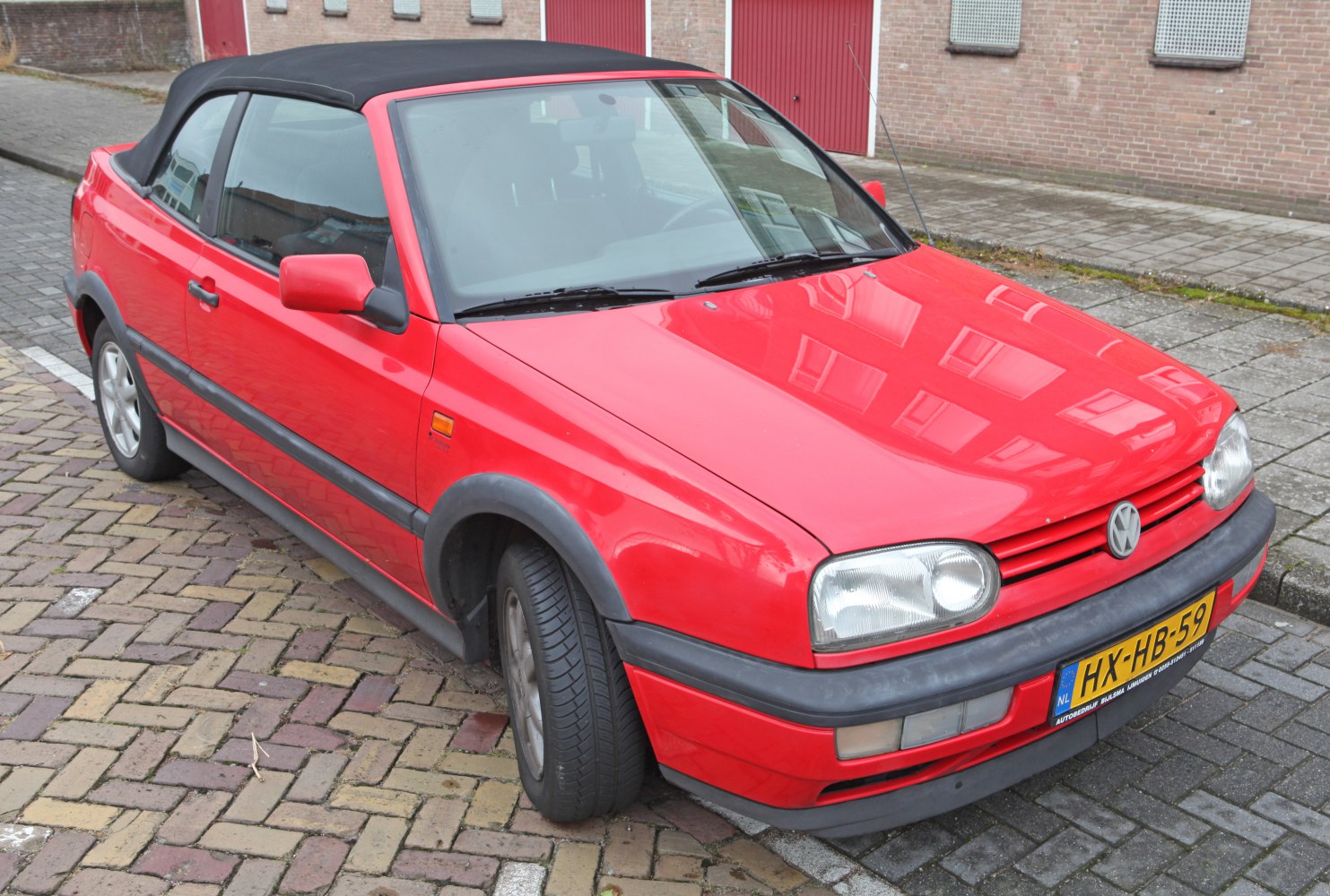 Red convertible with black soft top roof, front-side view
