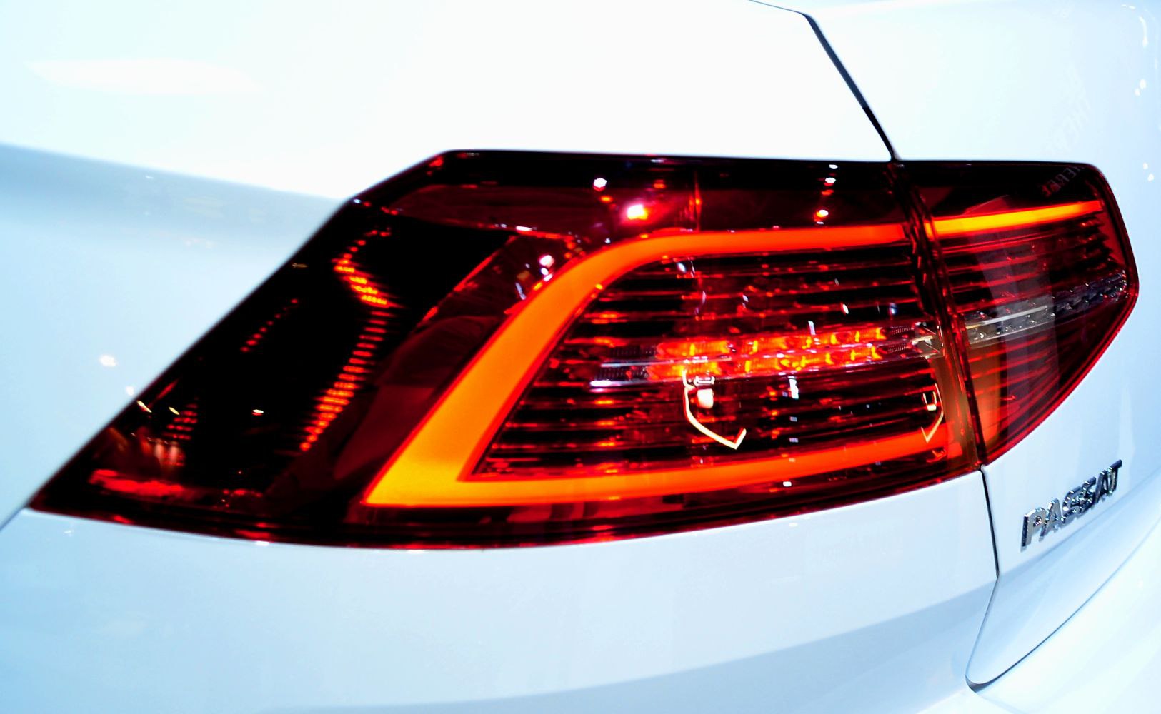 Close-up of modern rear LED tail light and badge on white vehicle.