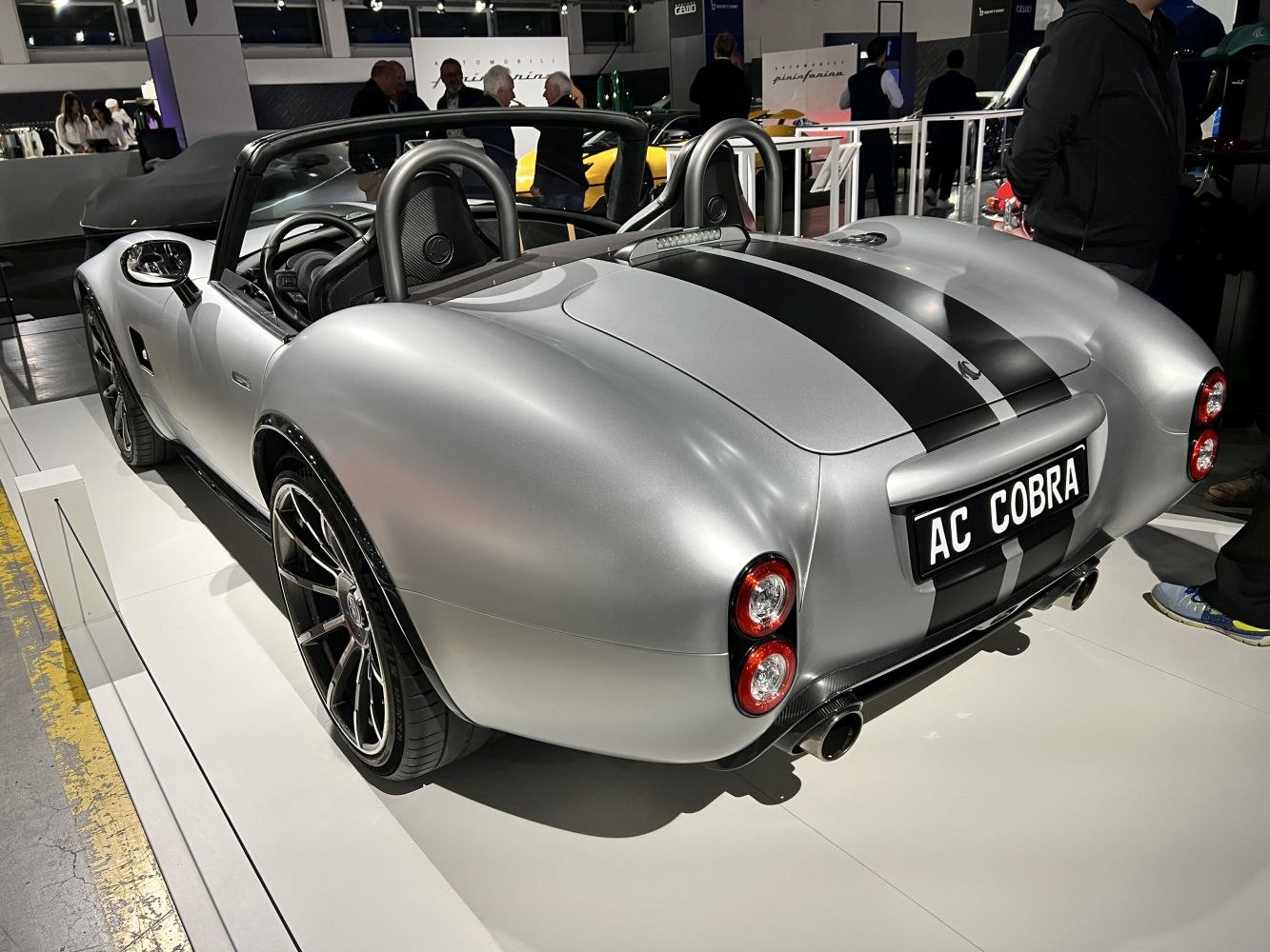 Rear view of a silver convertible with black racing stripes and dual round taillights