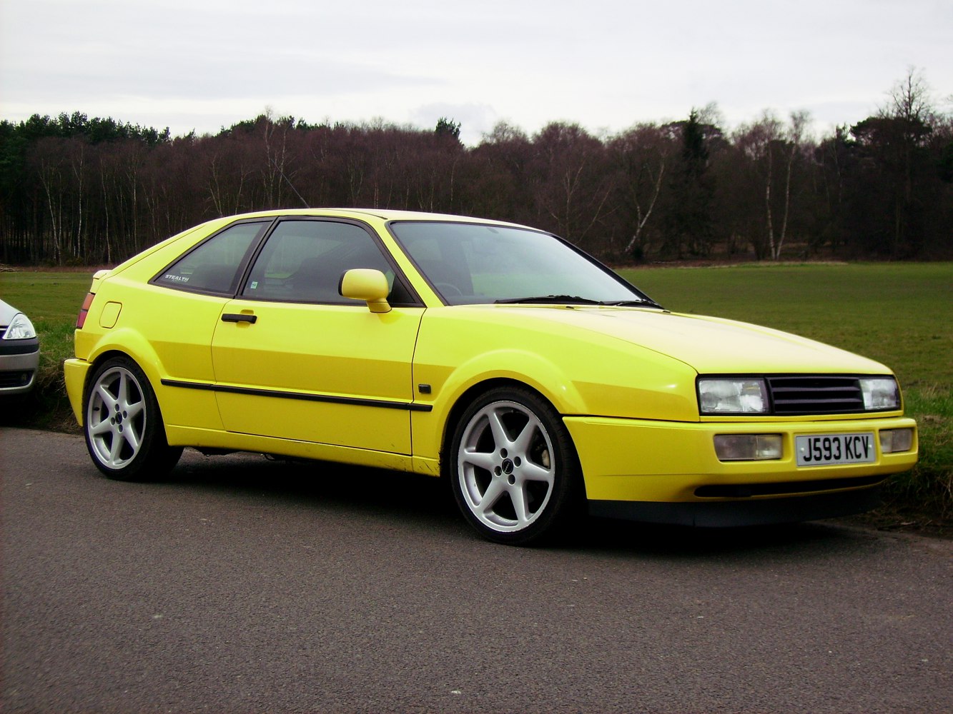 Yellow coupe with sporty wheels, side profile view on road