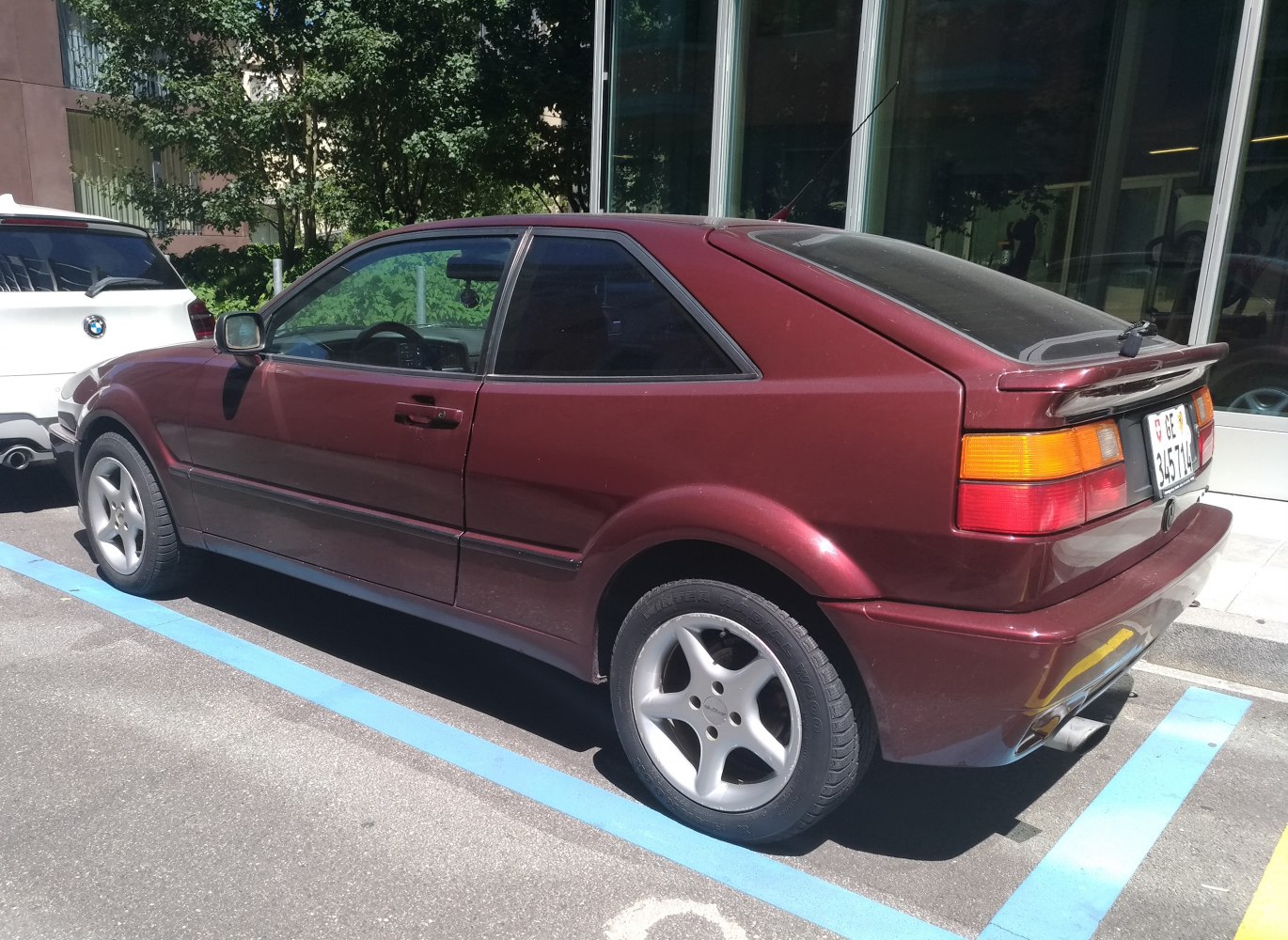 Rear-side view of a burgundy hatchback with rear spoiler and five-spoke wheels