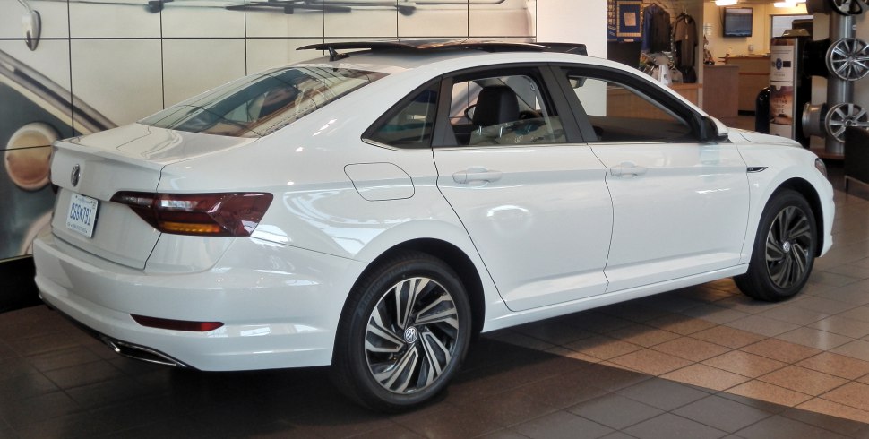 White sedan with alloy wheels and sunroof, rear and side view inside showroom