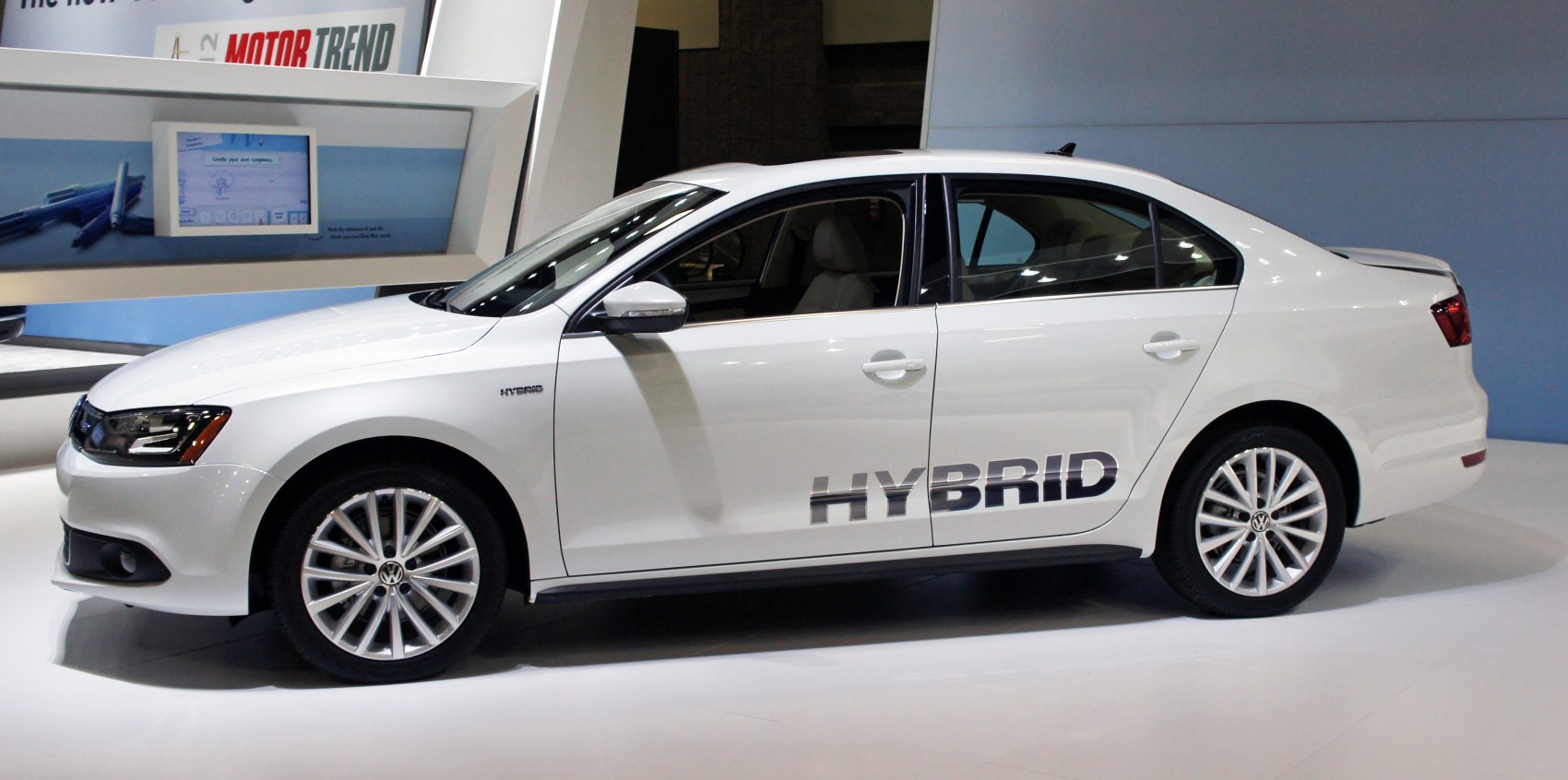 Side view of a white hybrid sedan with alloy wheels and 'HYBRID' decal.