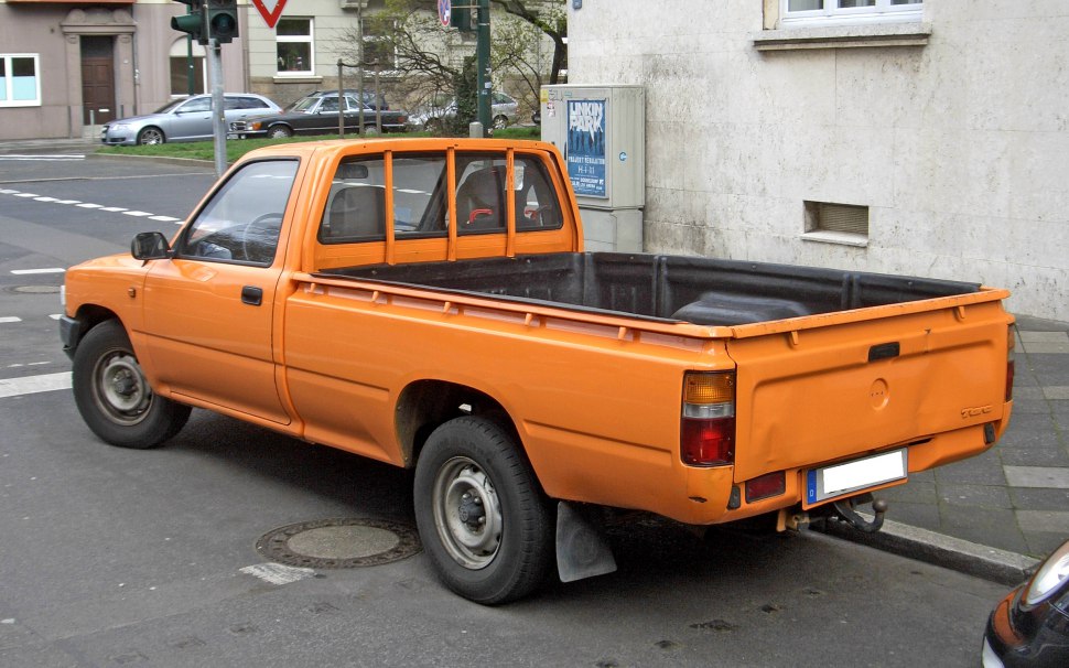 Orange pickup truck with single cab and open cargo bed from rear side