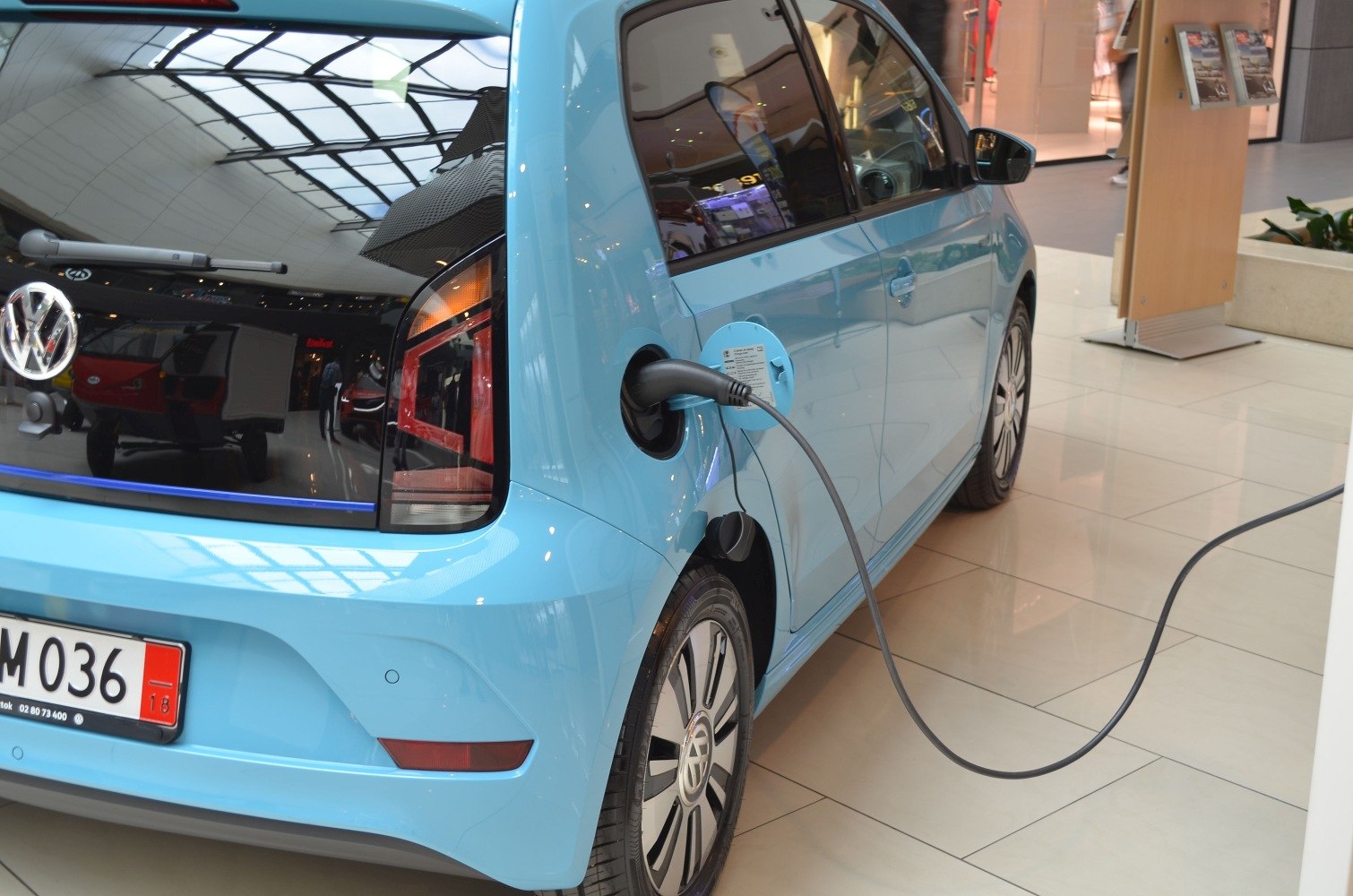 Blue electric hatchback plugged into charger, rear-side view.