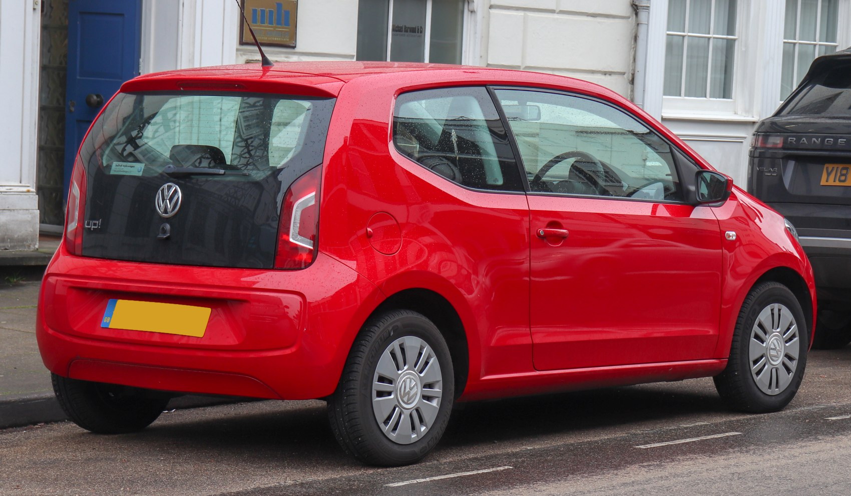 Compact red hatchback showing rear hatch and side profile with distinctive window design.