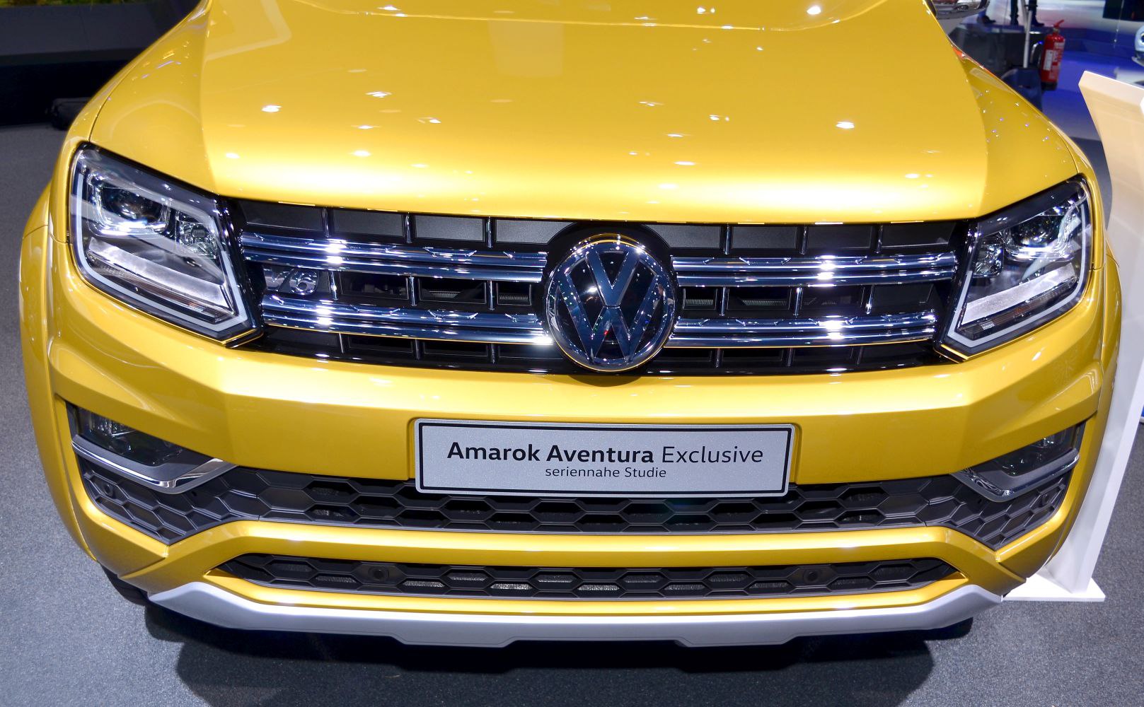 Yellow vehicle front with chrome grille and modern headlights