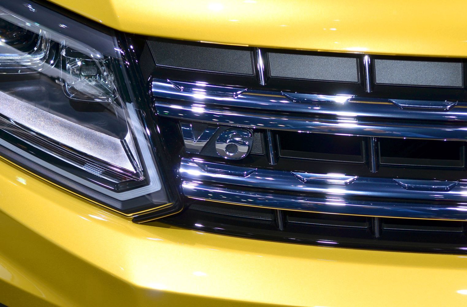 Chrome V6 grille and modern headlight detail on yellow vehicle front