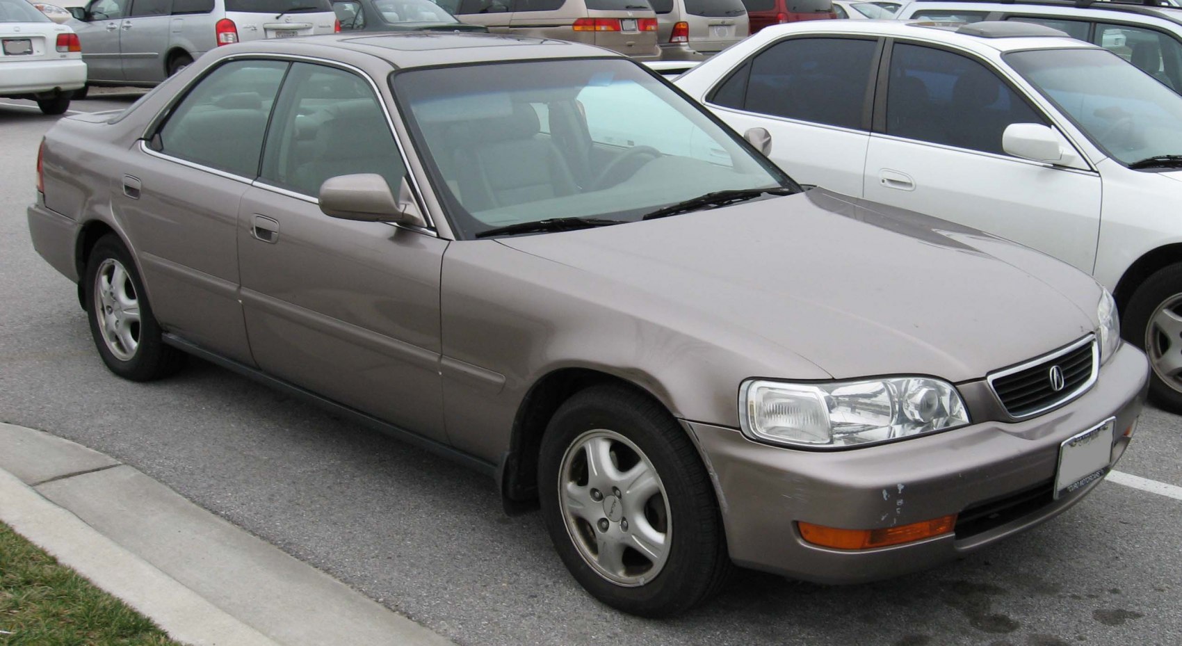 Front side view of a mid-90s sedan with alloy wheels parked in an urban lot