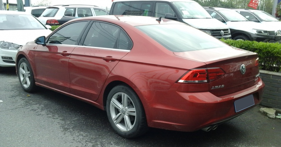 Red sedan rear side with tinted windows and alloy wheels.