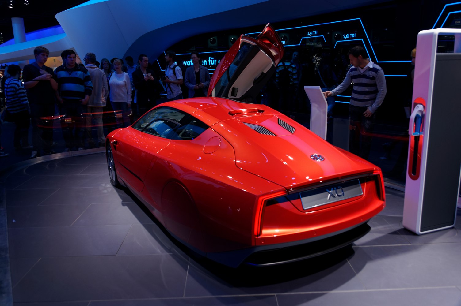 Aerodynamic red hybrid coupe with gull-wing door open from the rear corner.