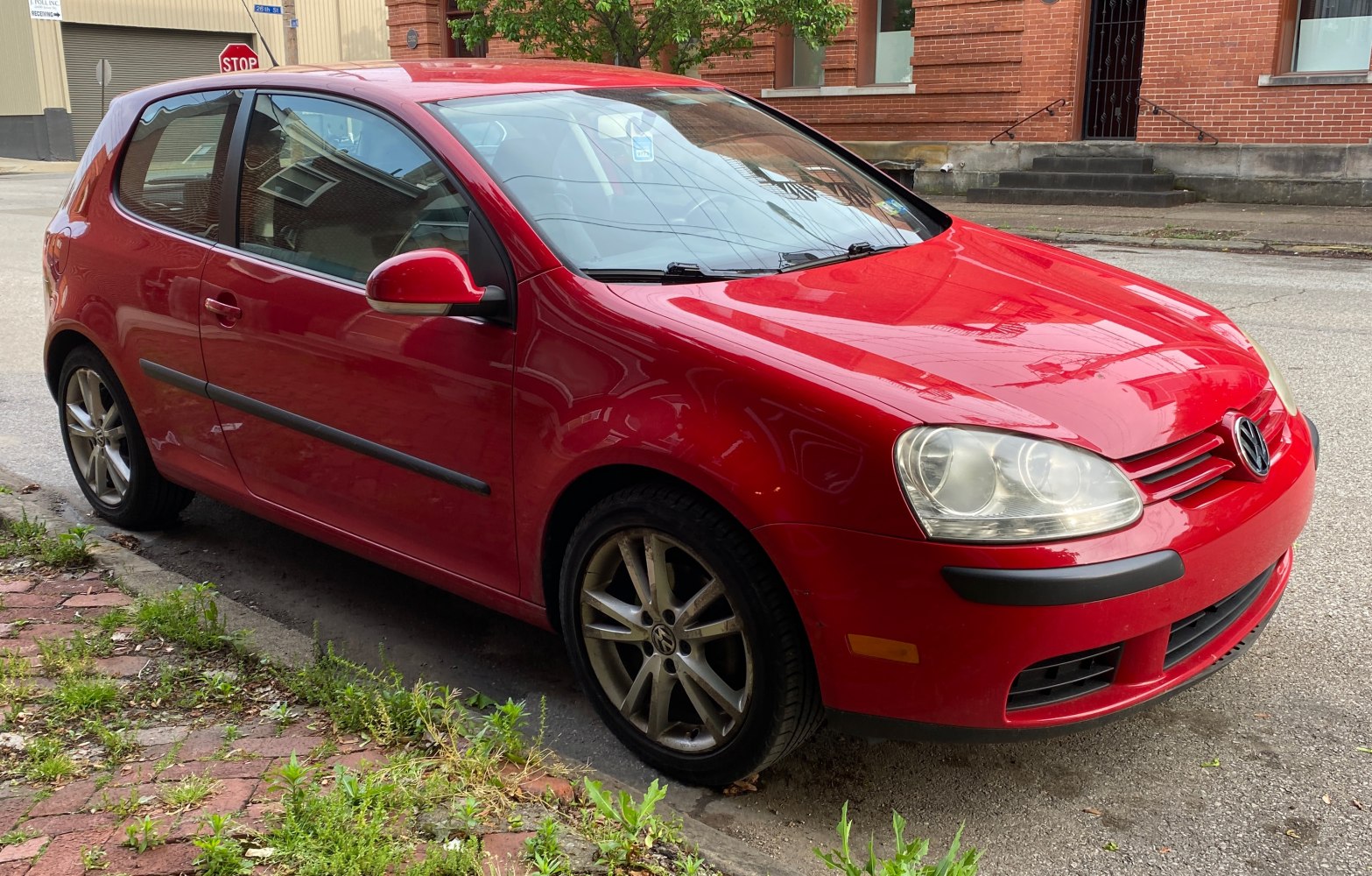Red 3-door hatchback with alloy wheels parked on street curb