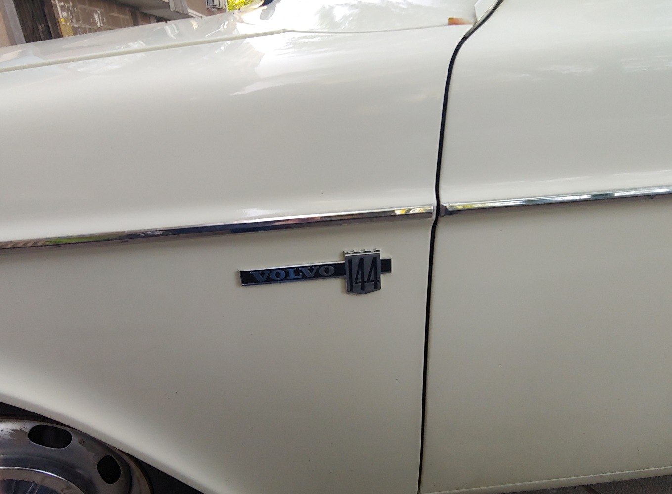 Close-up of classic Volvo 144 side emblem and chrome door trim on white panel